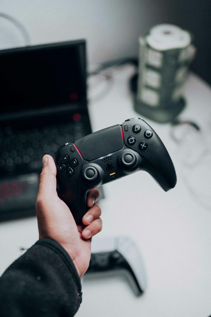 Close-up shot of a hand holding a black game controller near a laptop, showcasing gaming technology.